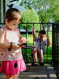 Cute girl with toy against playful brother on railing at porch