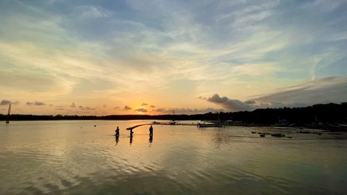 Silhouette people in sea against sky during sunset