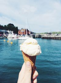 Close-up of hand holding ice cream cone against lake