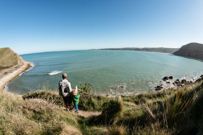 Father and young child looking down at ocean from mountain trail