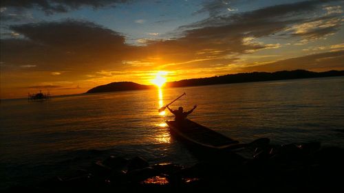 Silhouette man in sea against sky during sunset