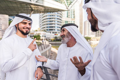 Senior man with grandsons wearing dish dash standing against buildings in city