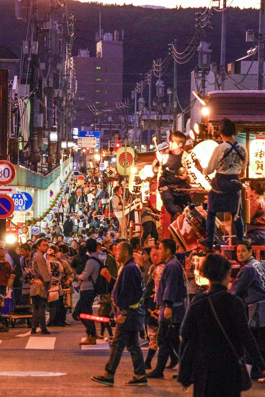 PEOPLE STANDING ON ROAD AGAINST CITYSCAPE