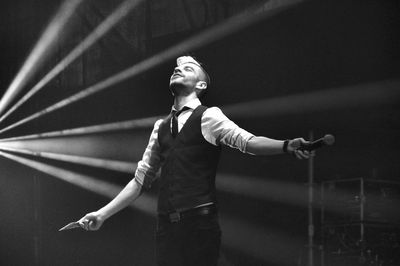 Mature man with arms outstretched standing on stage in music concert