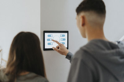 Rear view of brother and sister using digital tablet mounted on wall at home