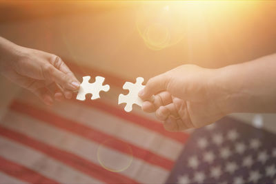 Cropped hands of people holding jigsaw pieces against american flag