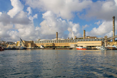 View of city at waterfront against cloudy sky