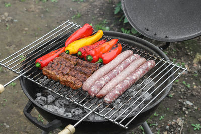 Raw sausages, cutlets and peppers on the grill grate.