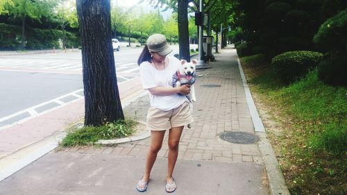 Mid adult woman with dog standing on footpath at park