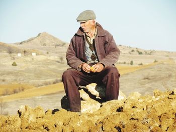 Senior man sitting on rock against clear sky