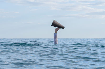 Cropped image of a hand with a megaphone into the  sea against sky