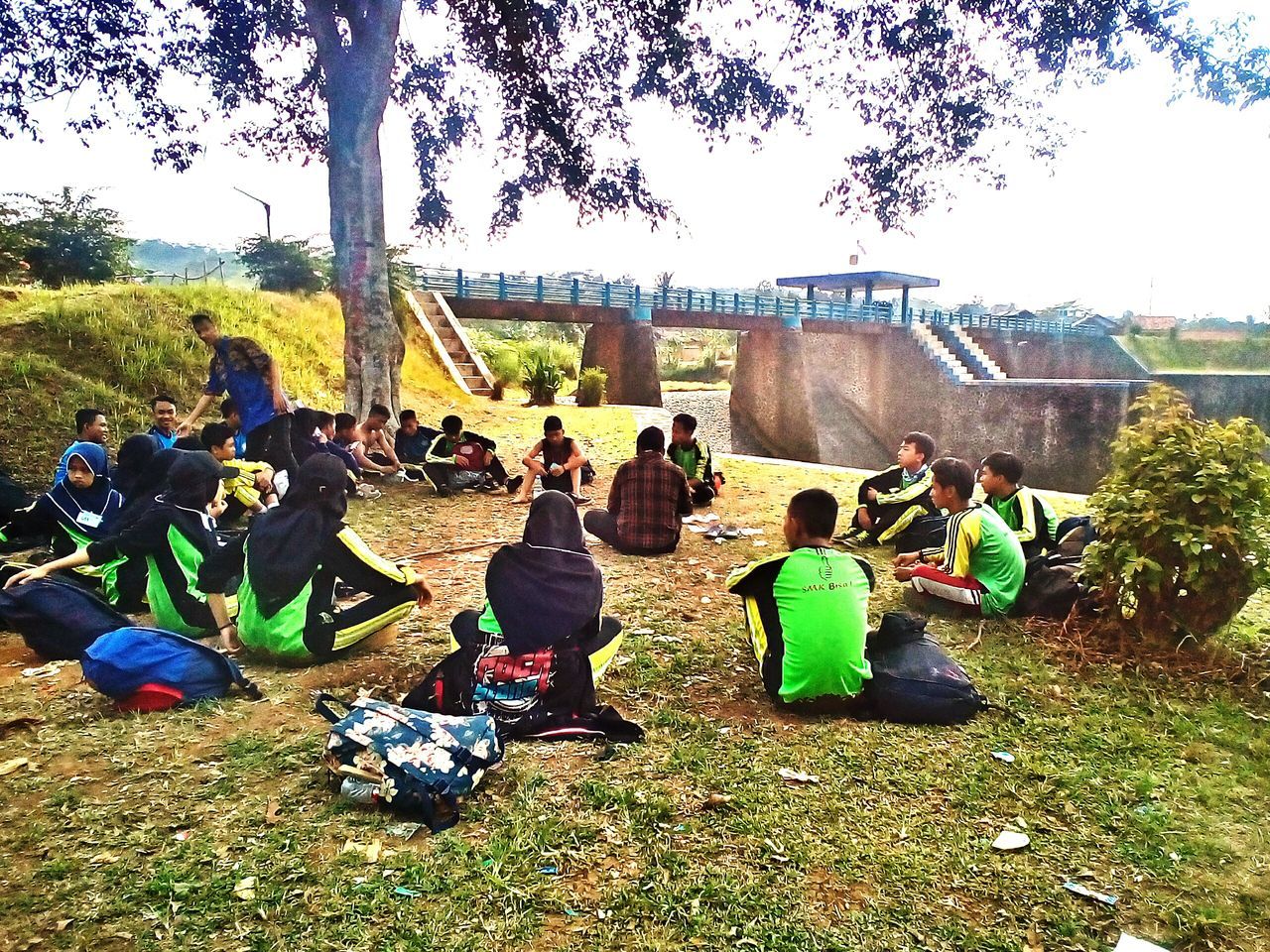 group of people, real people, tree, plant, large group of people, architecture, women, crowd, sitting, nature, day, built structure, men, sky, grass, lifestyles, leisure activity, relaxation, building exterior, outdoors