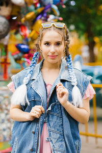 Young woman with blue pigtails in a denim vest in an amusement park