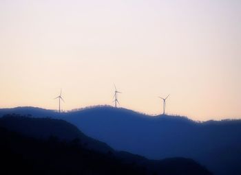 Wind turbines on silhouette landscape against sky during sunset