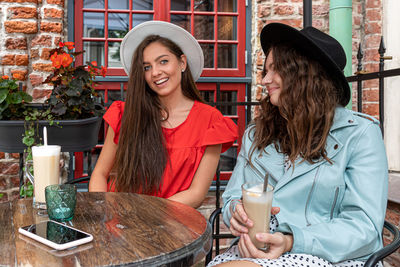 Two cheerful pretty young women drinking coffee, talking and laughing in outdoor cafe