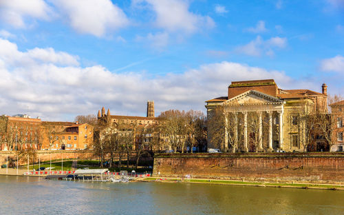 Buildings by river against cloudy sky