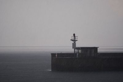 Lighthouse by sea against clear sky