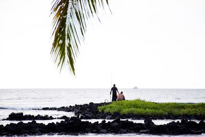 Men standing on beach against clear sky