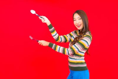 Portrait of smiling young woman standing against red background