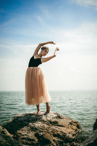 Woman standing on rock by sea against sky