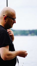 Bald man fishing in lake against sky