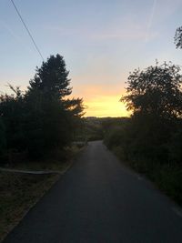 Road amidst trees against sky during sunset