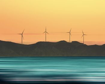 Wind turbines on field against sky during sunset