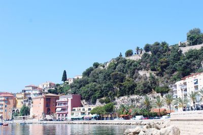 Scenic view of river by buildings against clear blue sky