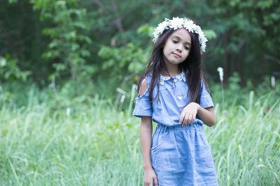 Cute thoughtful girl wearing flowers looking down while standing on grassy field