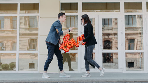 Side view of couple holding balloon standing against building