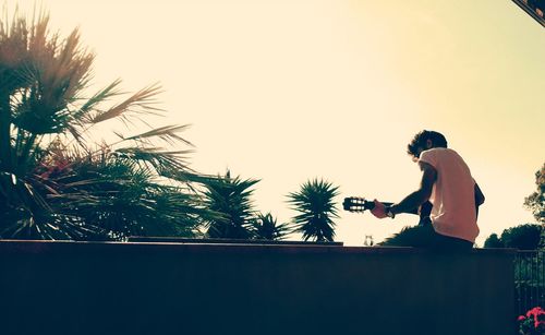 Low angle view of man standing by palm tree against clear sky