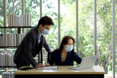 Colleagues wearing masks discussing over laptop on desk