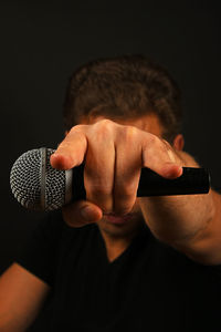 Musician holding microphone while showing rock sign against black background