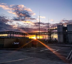 Road by factory against sky during sunset