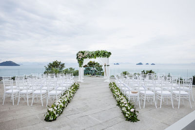 Empty chairs and table by sea against sky
