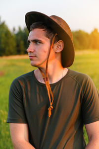 Young man serious farmer in cowboy hat at agricultural field on sunset with sun flare. profile 