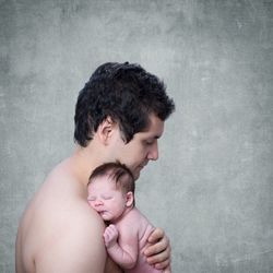 Side view of shirtless father carrying daughter against wall