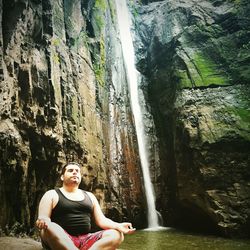 Low angle view of man meditating by waterfall