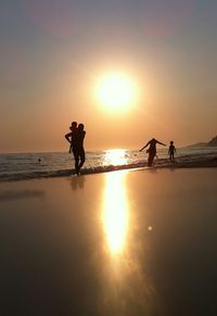 Silhouette people on beach against sky during sunset