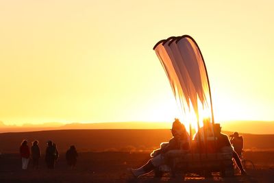 People sitting on land against sky during sunset