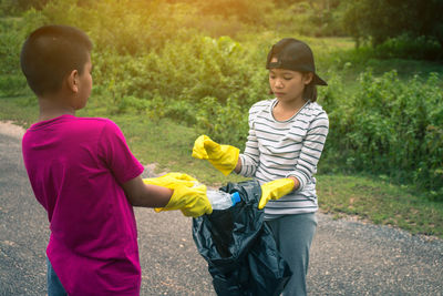 Siblings picking bottles from road against sky