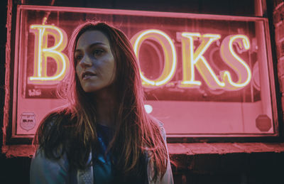 Thoughtful woman standing against red neon text at night