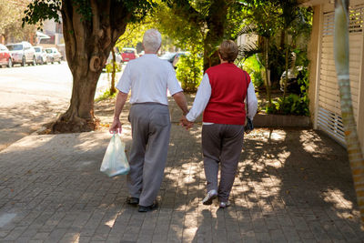 Rear view of senior couple holding hands while walking on sidewalk