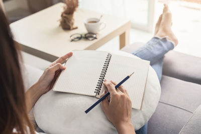 High angle view of woman writing in book at home