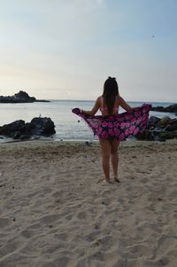 Rear view of woman standing on beach against sky