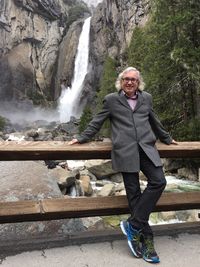 Portrait of smiling young woman standing against waterfall