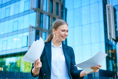 Business woman holding papers in her hands raised up, happy smiling