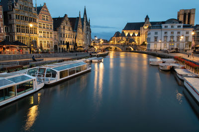 Sailboats moored on canal amidst buildings in city at dusk