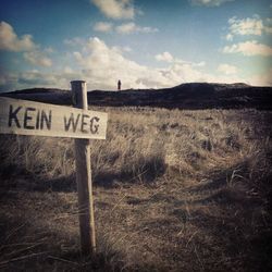 Information sign on field against cloudy sky