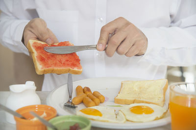 Midsection of man applying jam on bread